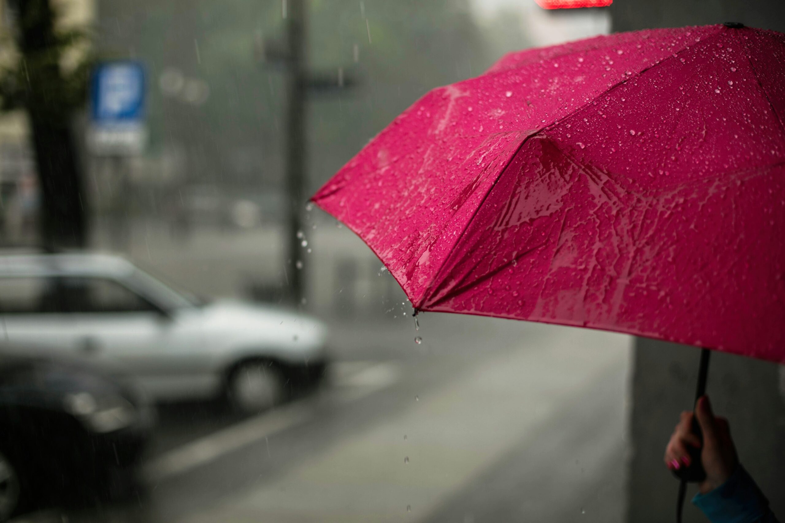 雨の中赤い傘を刺し車を見つめる人