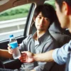 助手席の男性が運転手にドリンクを差し出す